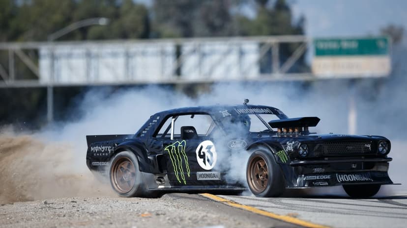 Black Ford Mustang Hoonicorn drifting on a road with thick white tire smoke and spinning bronze wheels.
