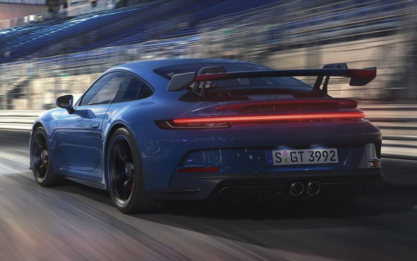 Blue Porsche 911 GT3 speeding on a professional racetrack with heavy motion blur and glowing red taillights.