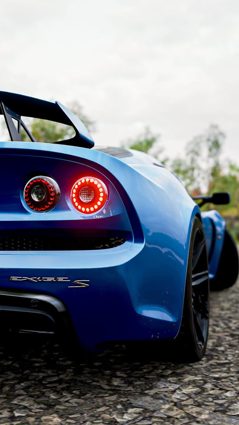 Blue Lotus Exige S rear view featuring glowing red LED taillights and a large spoiler on a rocky gravel surface.