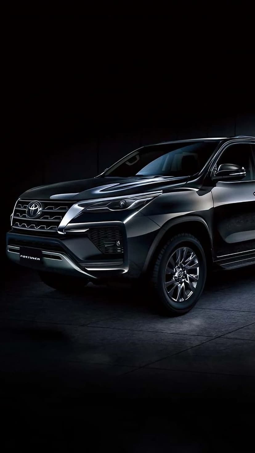 Toyota Fortuner SUV in black with glowing headlights and a detailed grille against a dark studio background.
