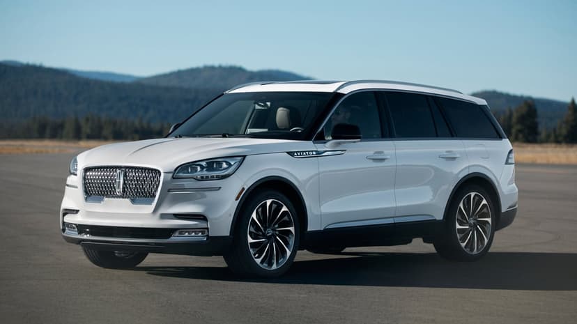 White Lincoln Aviator luxury SUV parked on asphalt with mountains and a clear blue sky in the background.