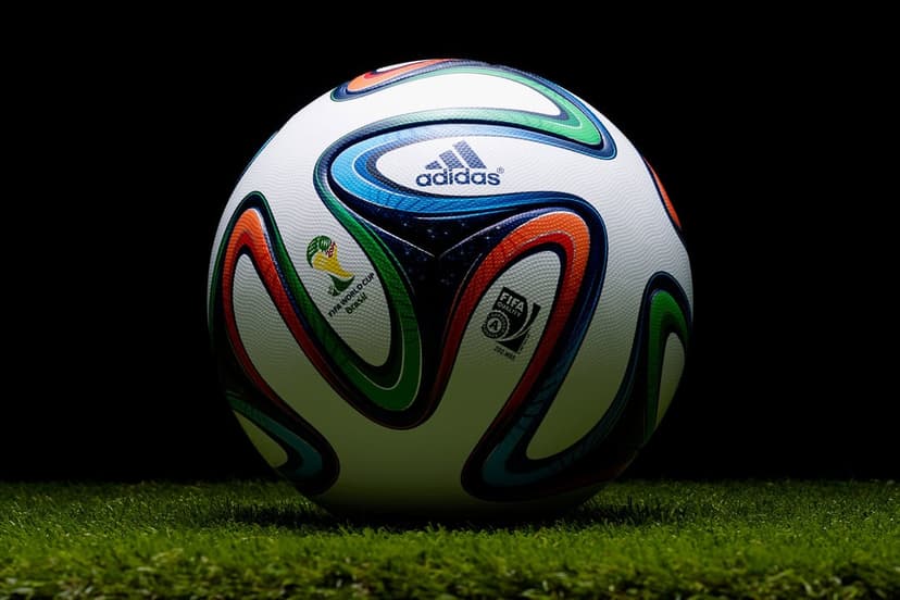 Adidas Brazuca soccer ball with colorful swirl patterns sits on green grass under soft studio lighting.