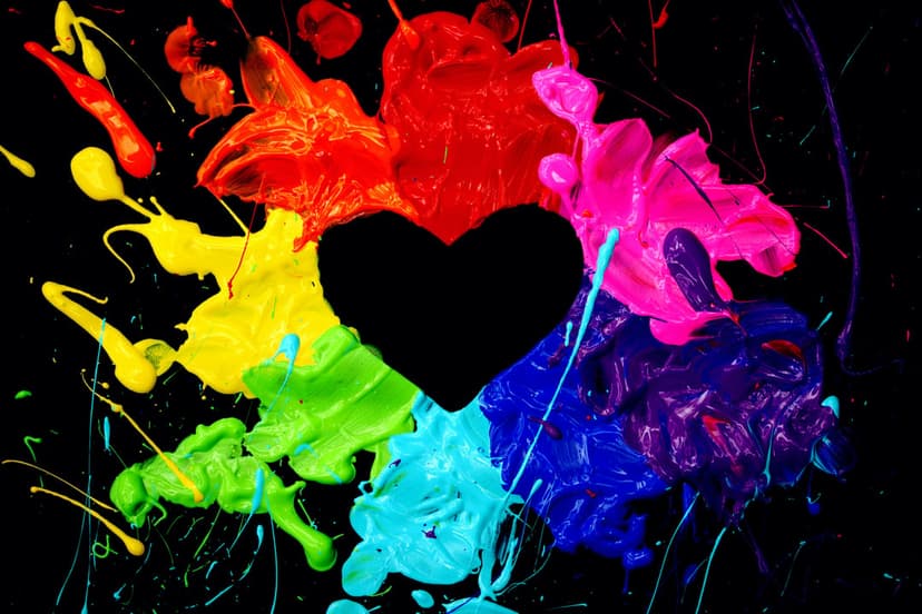 Black heart silhouette surrounded by an explosion of multi-colored rainbow paint drops on a dark background.
