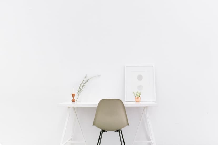 White minimalist desk paired with a tan ergonomic chair and circular abstract art against a bright wall.