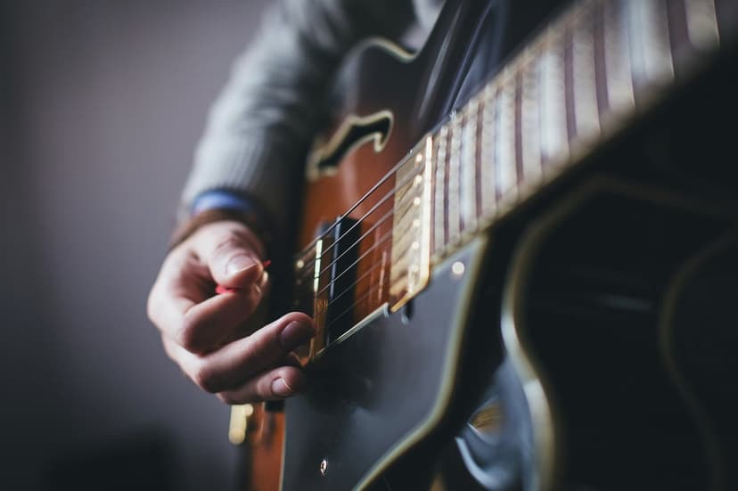Musician's hand gripping a pick and strumming strings on a wooden electric guitar with shallow depth of field.