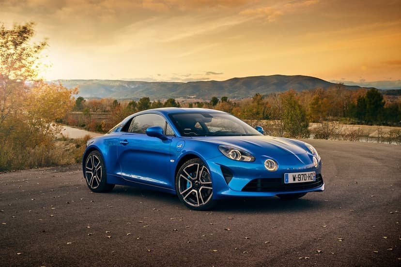 Blue Alpine A110 parked on a road at sunset with mountains and autumn trees in the background.
