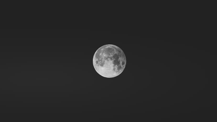 Full moon showing detailed craters and grey lunar plains against a pitch-black, starless night sky background.