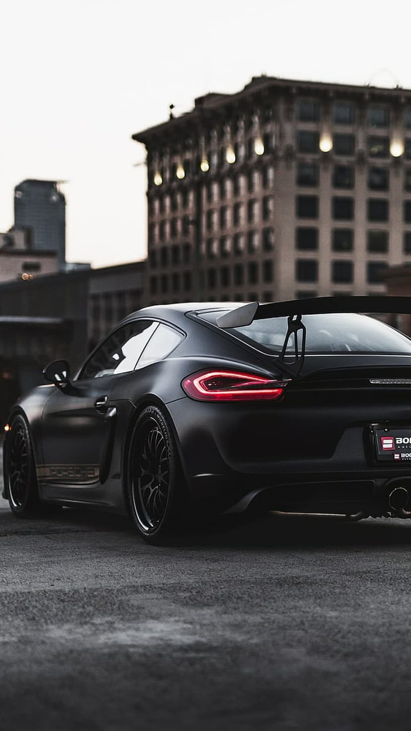 Porsche Cayman GT4 RS with a matte black finish and large rear wing parked on a cobblestone urban street.