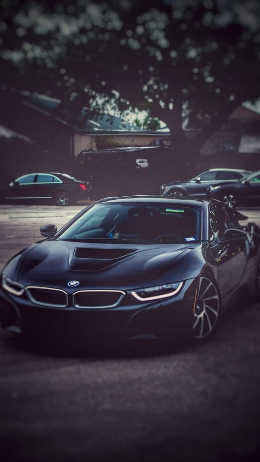 Black BMW i8 sports car with glowing LED lights parked on asphalt under a moody evening sky at twilight.