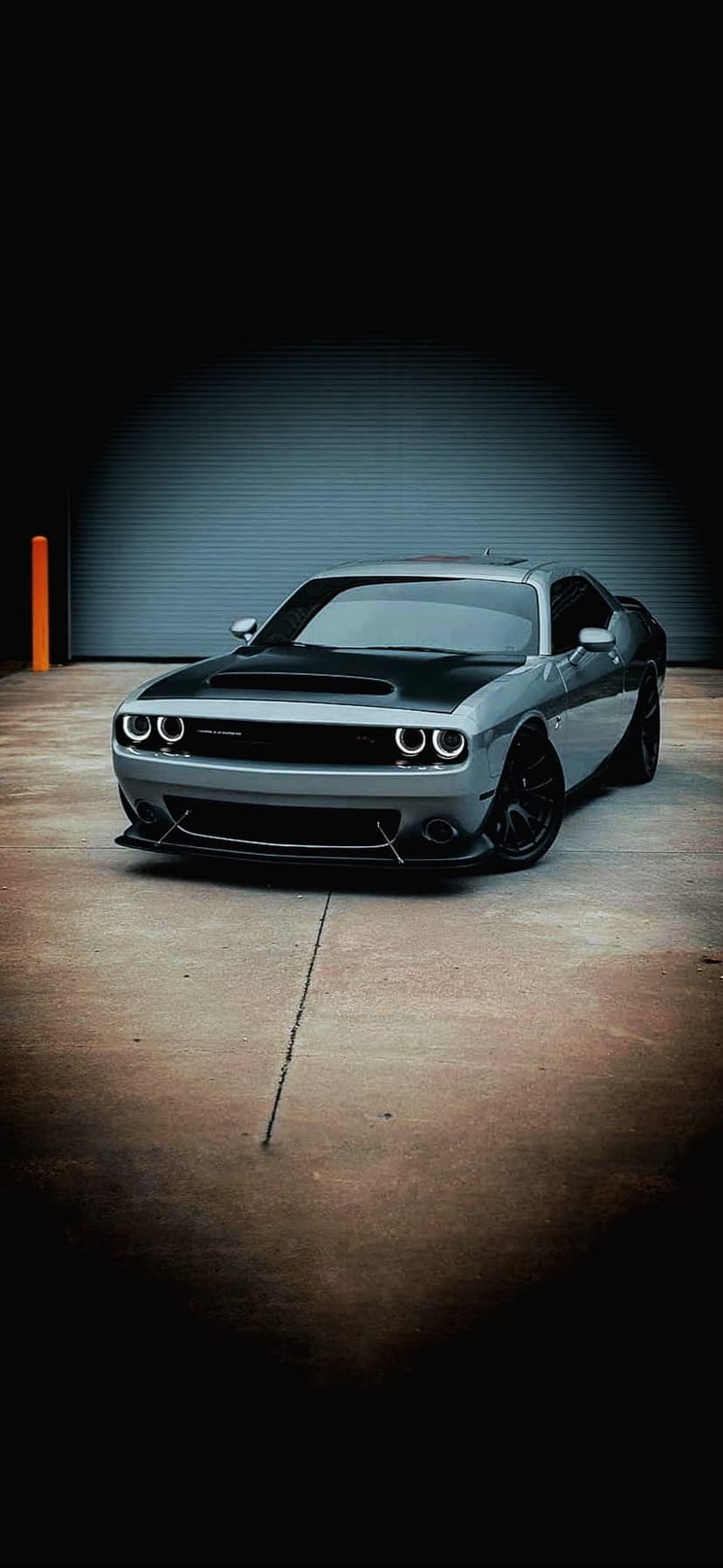 Dodge Challenger with glowing LED headlights and a matte black hood sits on a reflective concrete garage floor.