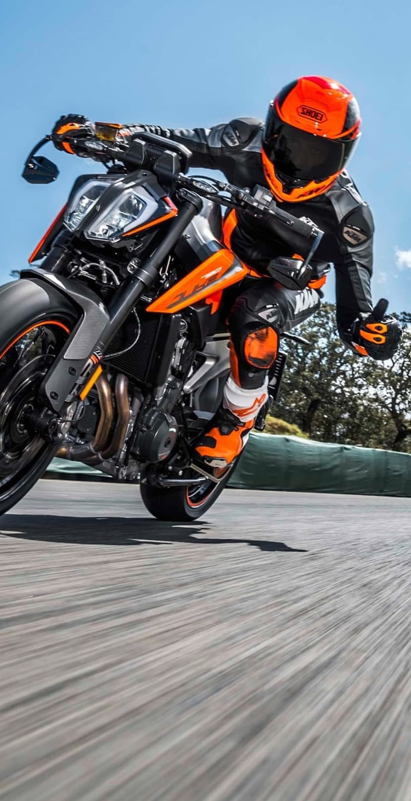 Professional racer in an orange helmet leans a KTM sportbike deep into a track curve against a clear blue sky.