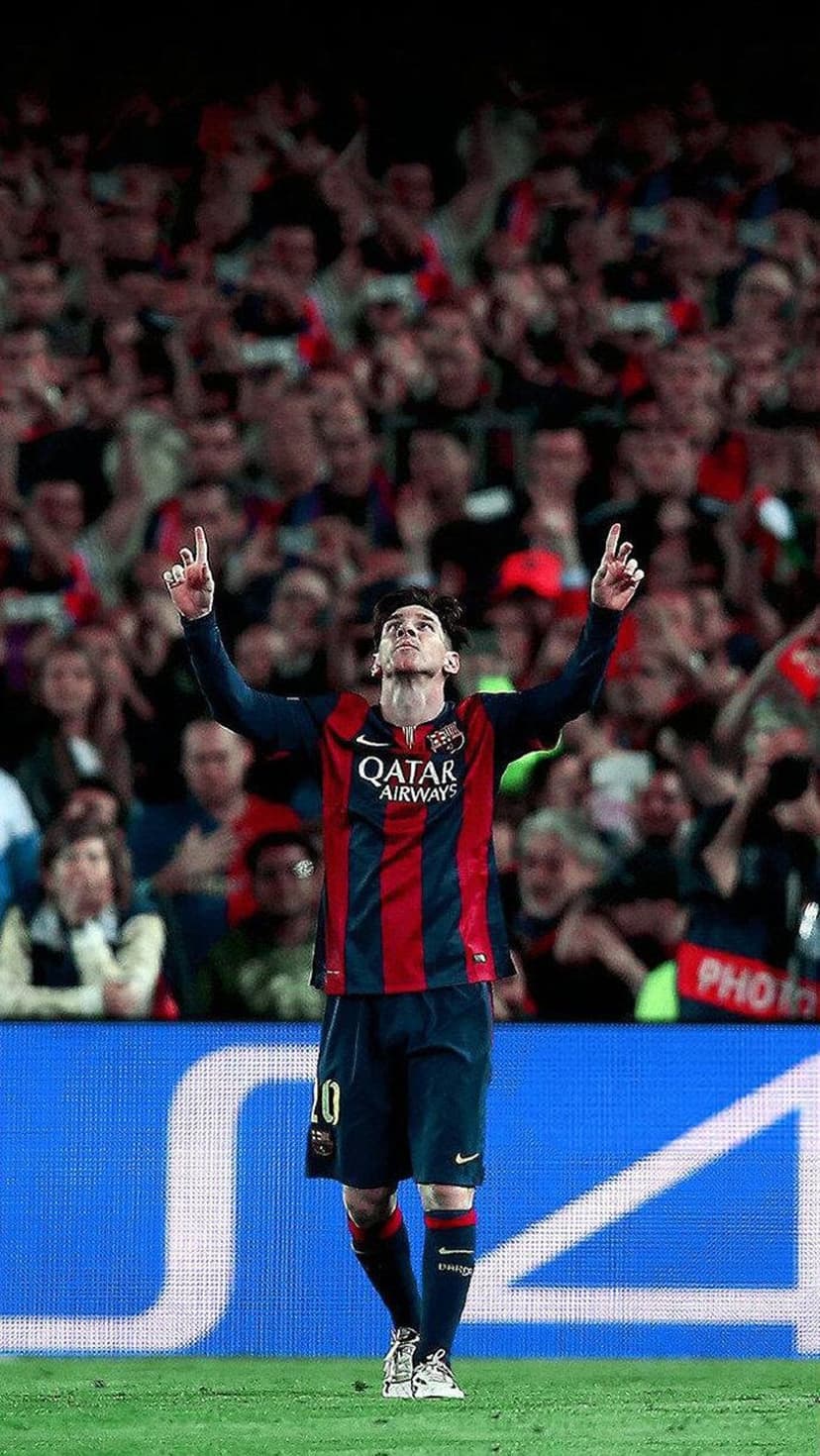 Lionel Messi raises both arms in a goal celebration while wearing a striped Barcelona jersey in a lit stadium.