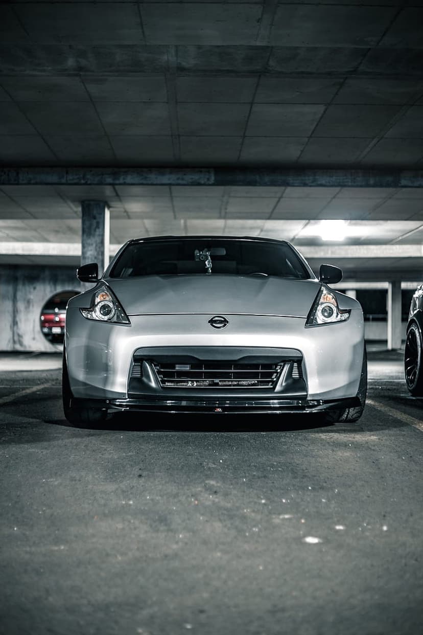 Silver Nissan 370Z sports car parked in a concrete garage with industrial lighting and aggressive front grille.