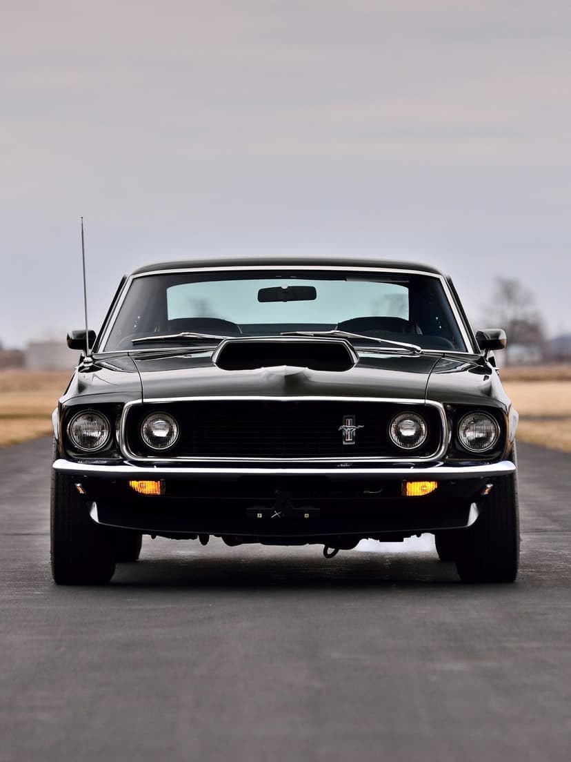 Front view of a black 1969 Ford Mustang with quad headlights and chrome bumper on an open asphalt road.