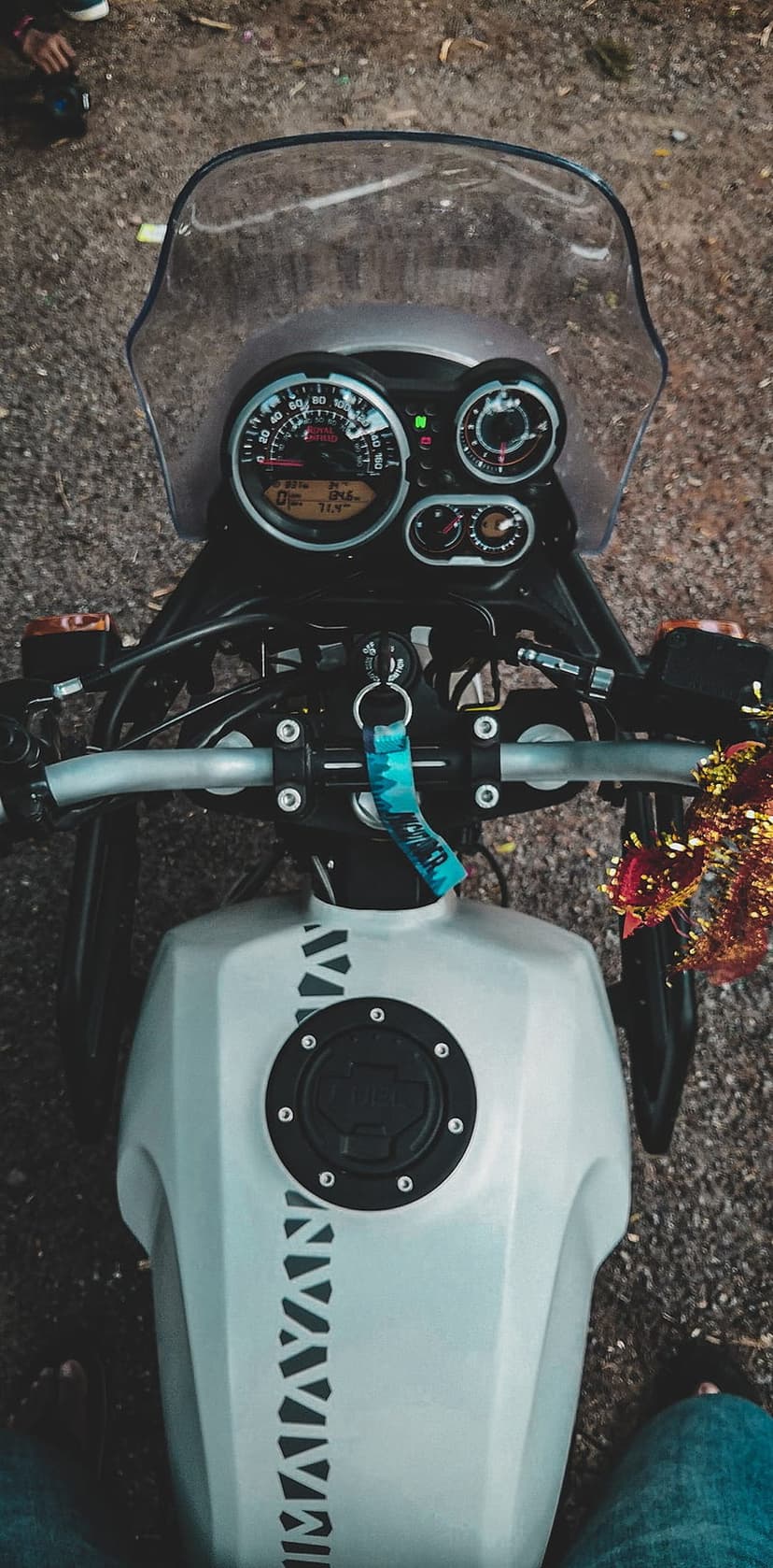Royal Enfield Himalayan motorcycle cockpit featuring a white fuel tank, speedometer gauges, and a clear windshield.