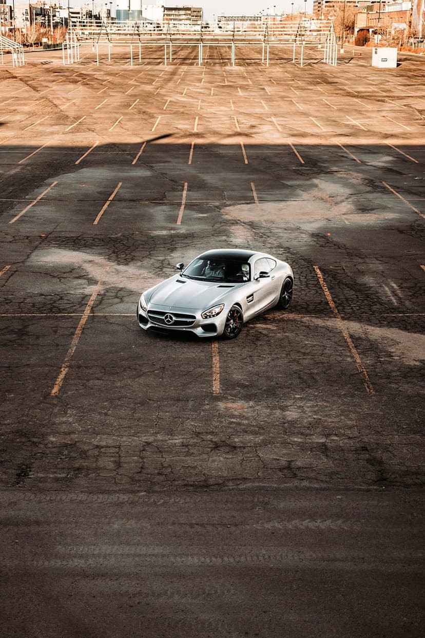 Mercedes-AMG GT S sports car viewed from above on a cracked parking lot with faded yellow lines and a bright sky.