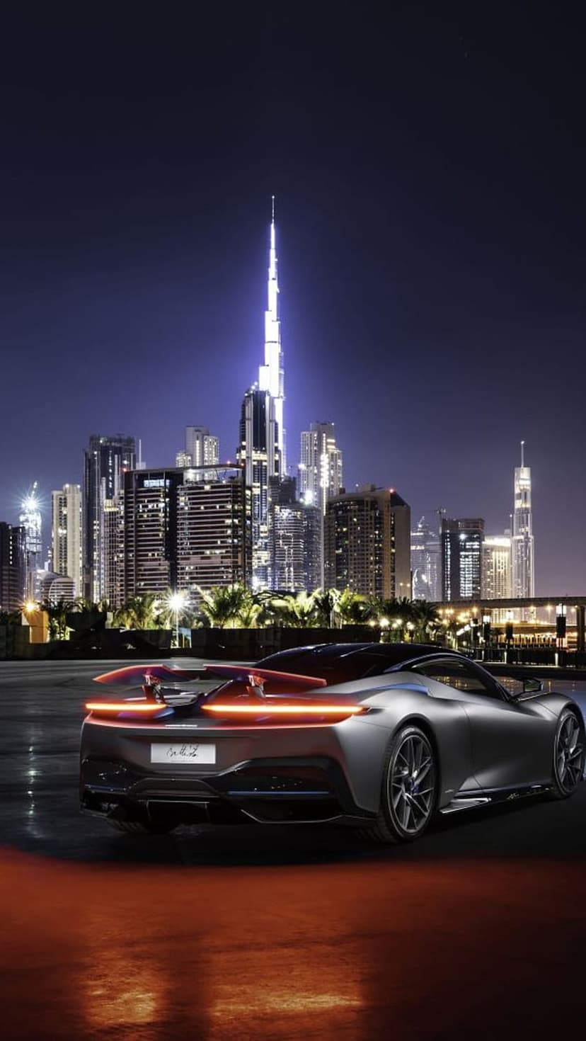 Modern sports car with glowing taillights parked on wet pavement against the illuminated Dubai city skyline.