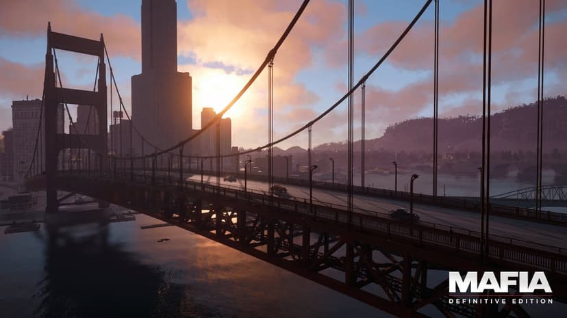 Large suspension bridge over water with vintage cars and city skyscrapers silhouetted against a warm sunset sky.