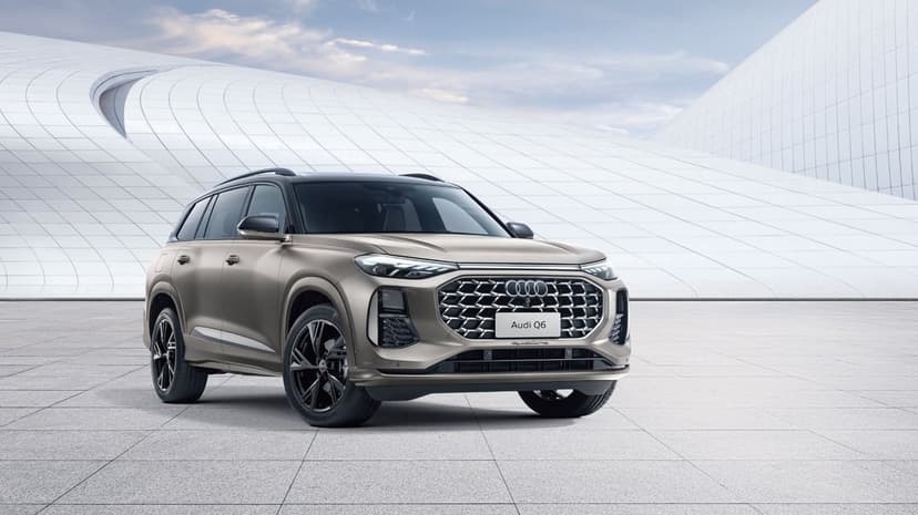 Audi Q6 luxury SUV parked on a tiled plaza in front of curved white modern architecture under a cloudy sky.