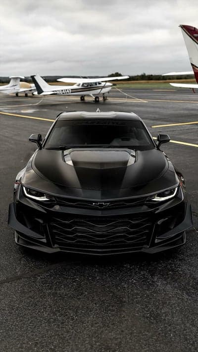 Black Camaro on Tarmac with Airplanes at Airport