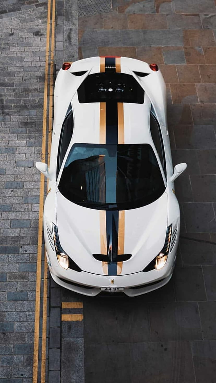 White Ferrari with navy and gold stripes parked on cobblestones seen from a direct overhead bird's eye view.