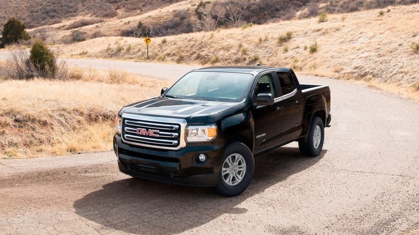 Black GMC Canyon pickup truck parked on a curved paved road surrounded by dry golden hills and sparse bushes.