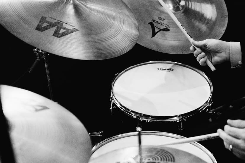 Drummer hands grip sticks while hitting a snare and cymbals in a detailed black and white close-up shot.