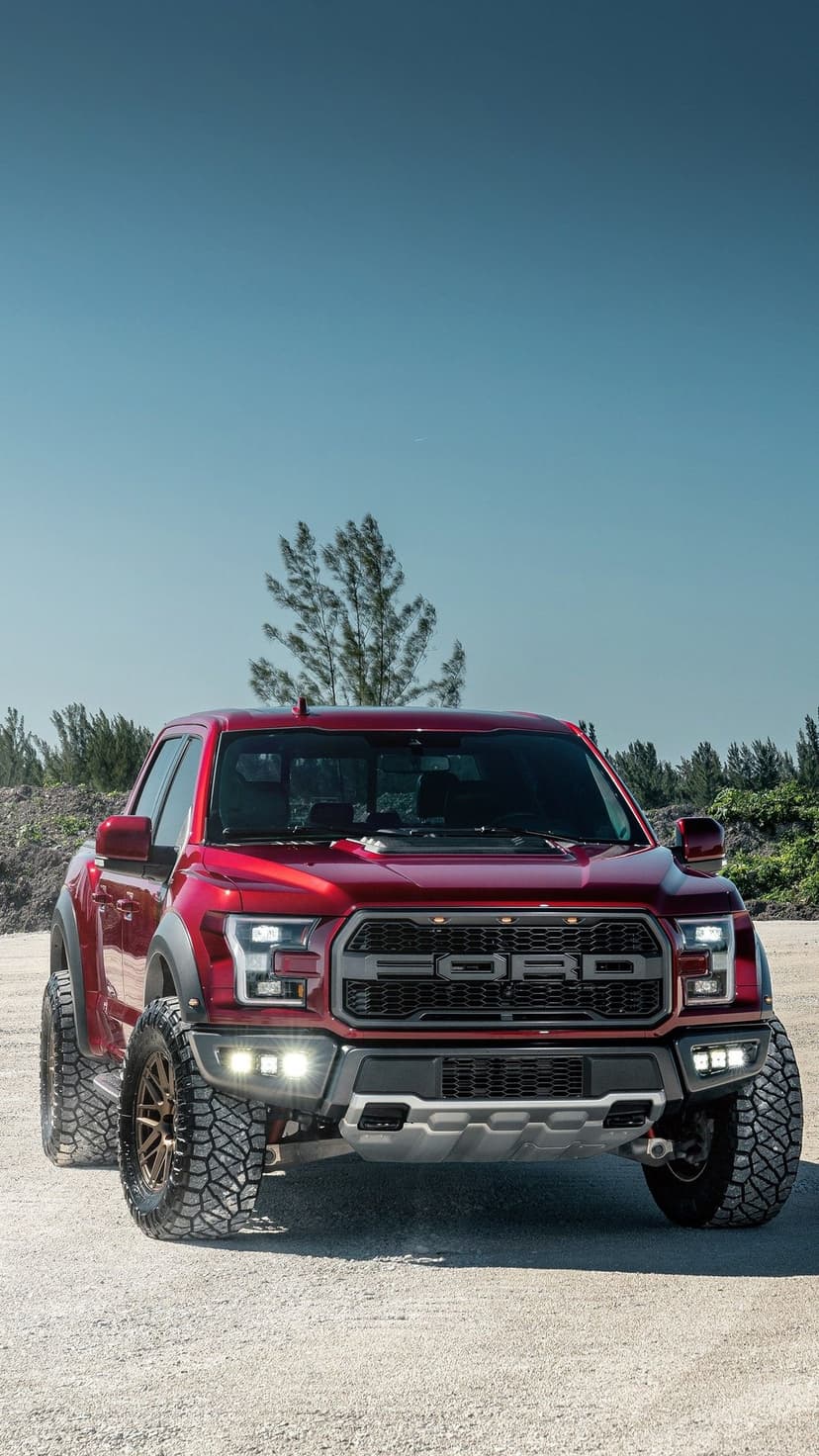 Red Ford Raptor truck with bronze wheels and glowing LEDs on a sandy plain under a bright blue sky.