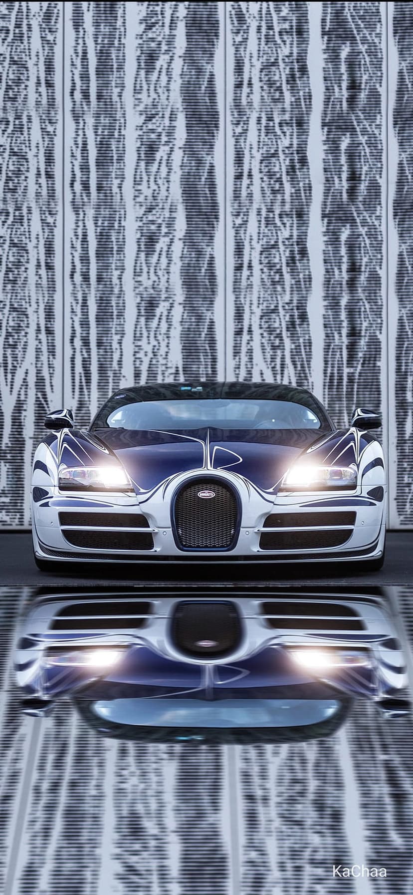 Bugatti Veyron in blue and white reflects on a polished floor against a textured wall with illuminated headlights.