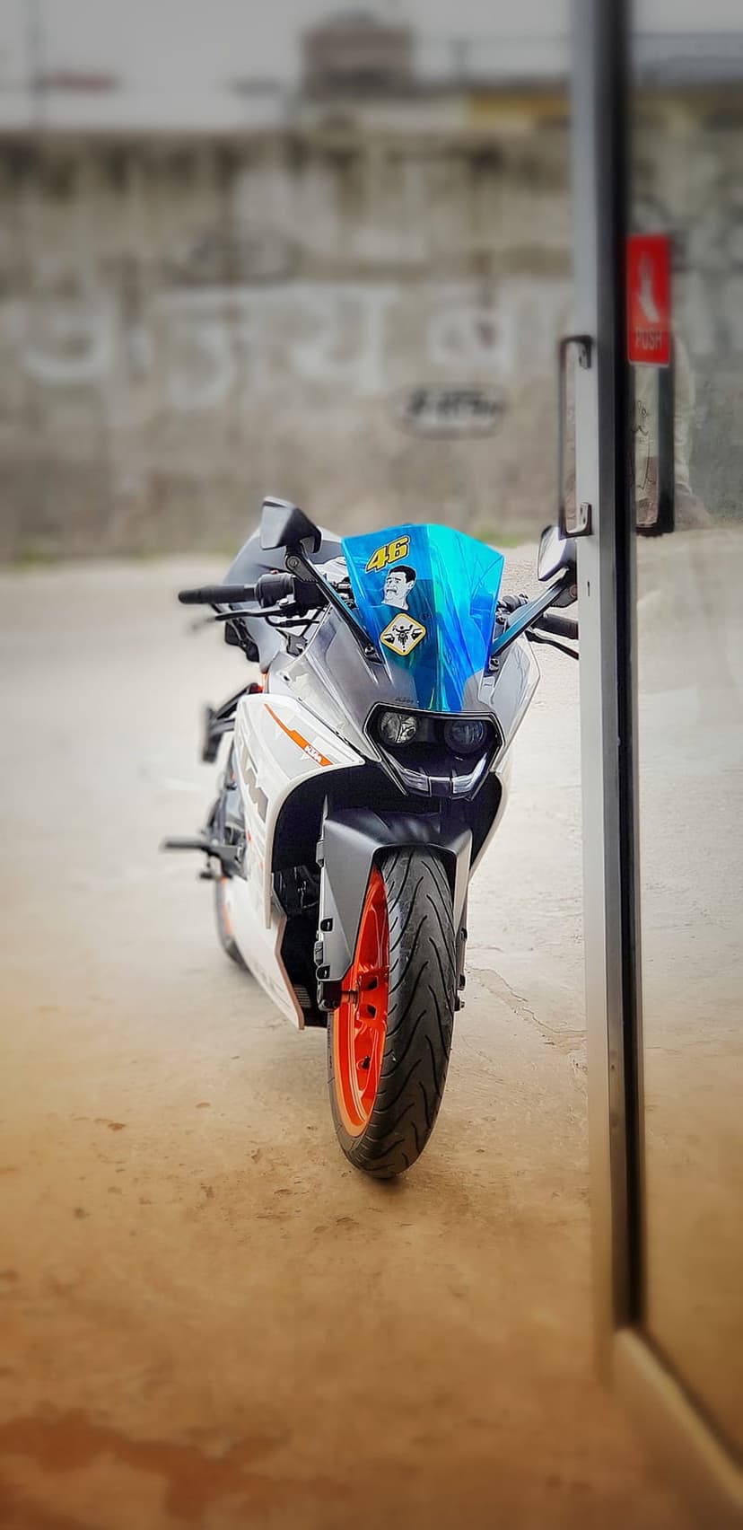 KTM RC 390 motorcycle with orange wheels and a blue windshield featuring a 46 sticker against a textured wall.