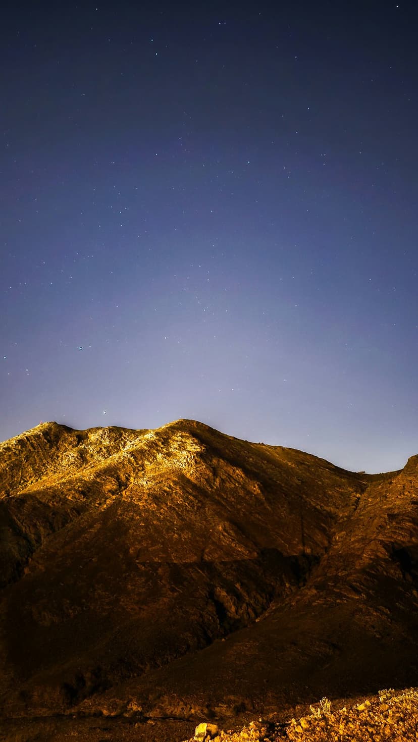 Jagged mountain peaks glowing with golden light under a dark blue sky filled with numerous twinkling stars.