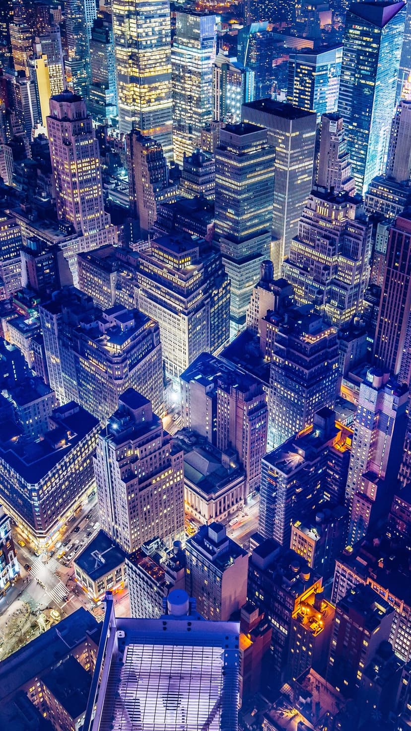 Glowing skyscrapers and city streets seen from an aerial view at night with a dense vertical grid pattern.