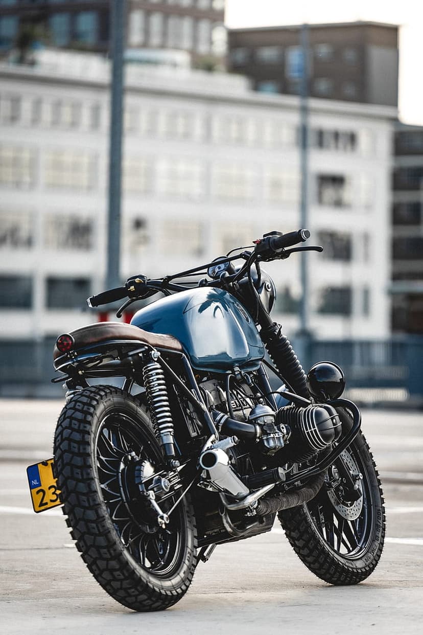 BMW R nineT motorcycle with a blue tank and tan leather seat parked on an urban street with blurred buildings.
