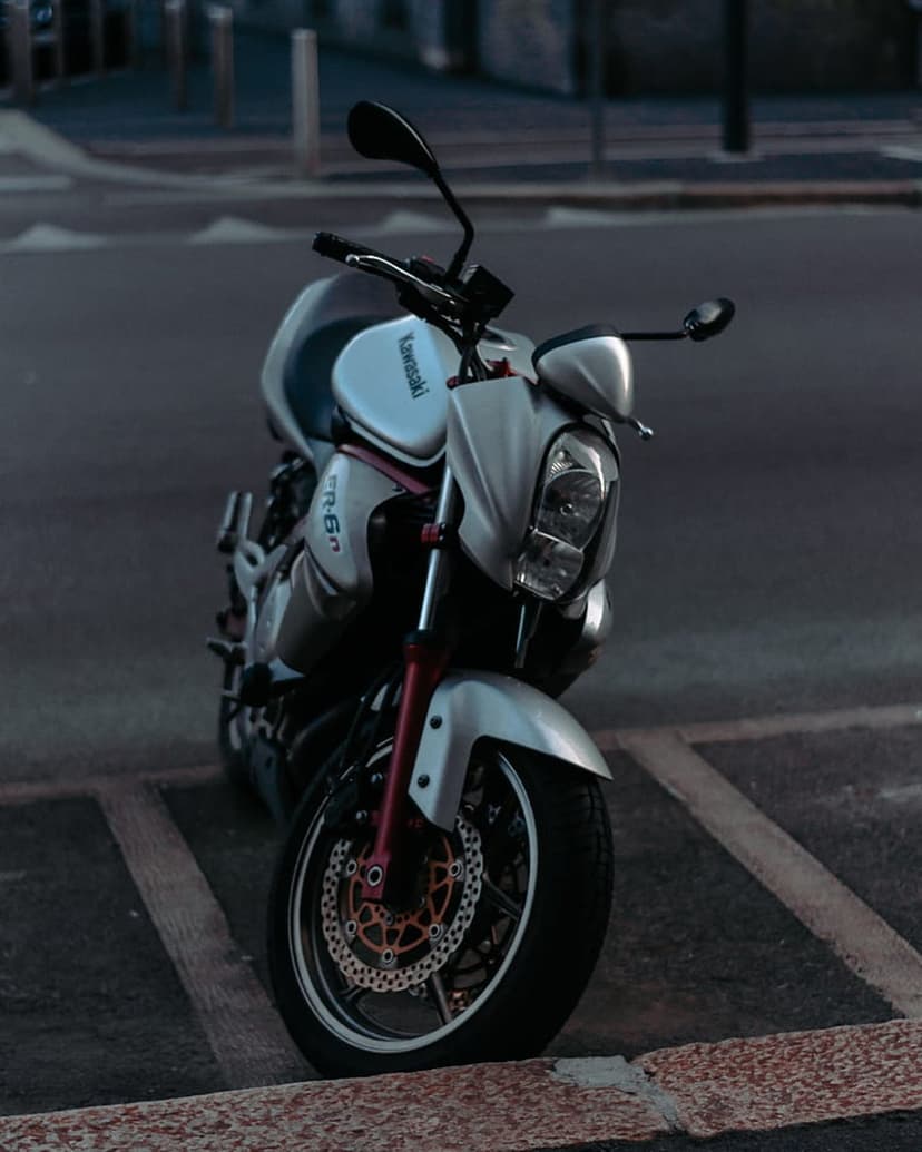 Kawasaki motorcycle with silver fairings and red fork accents parked on a paved city road with blurred buildings.
