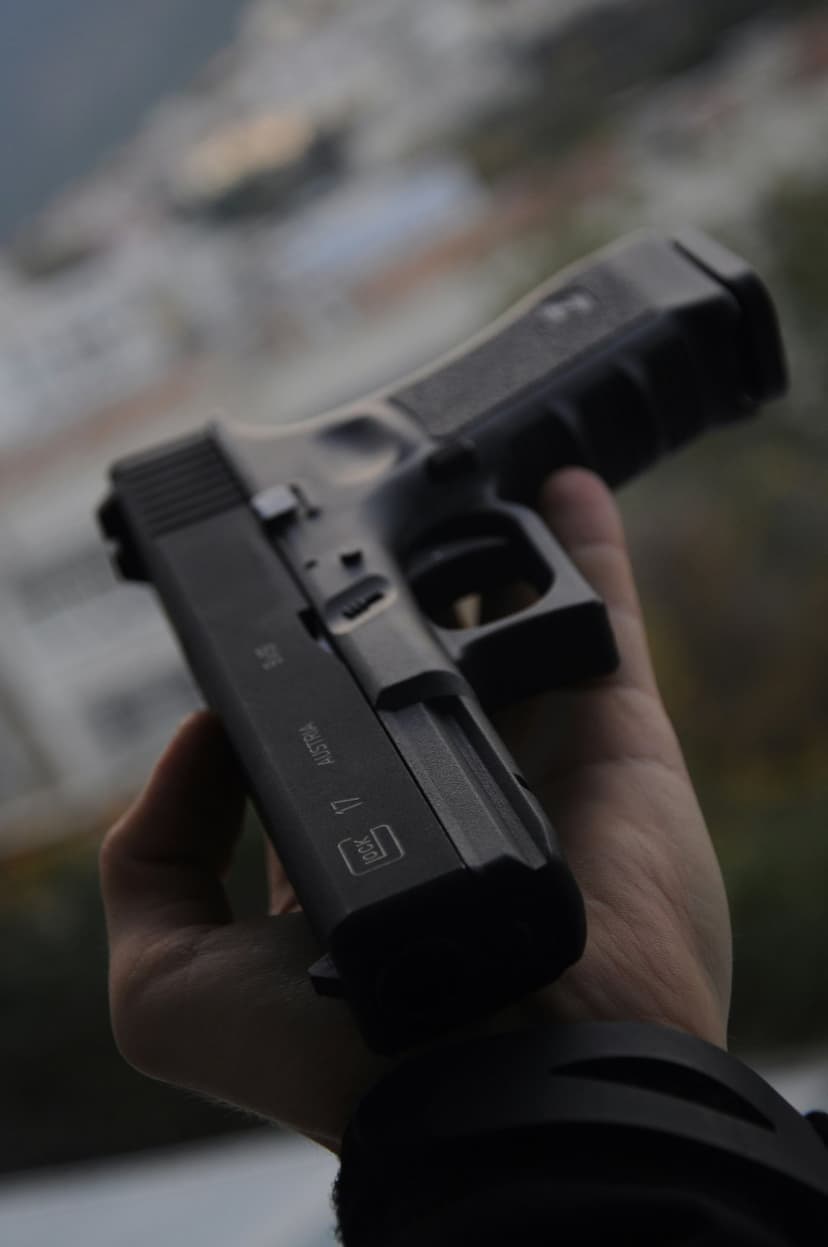 Black Glock 17 pistol held by a hand shows clear slide markings against a blurred outdoor city background.