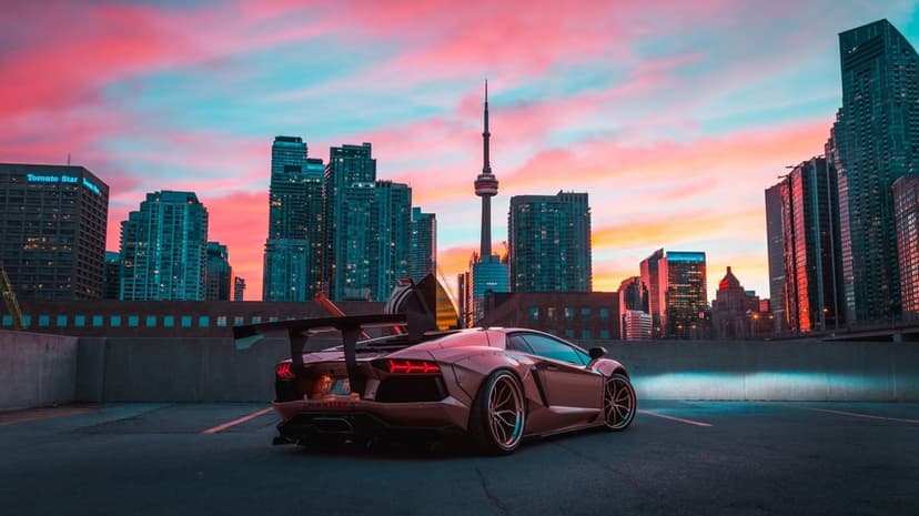 Widebody Lamborghini Aventador with a large spoiler on a Toronto rooftop under a pink and orange sunset sky.