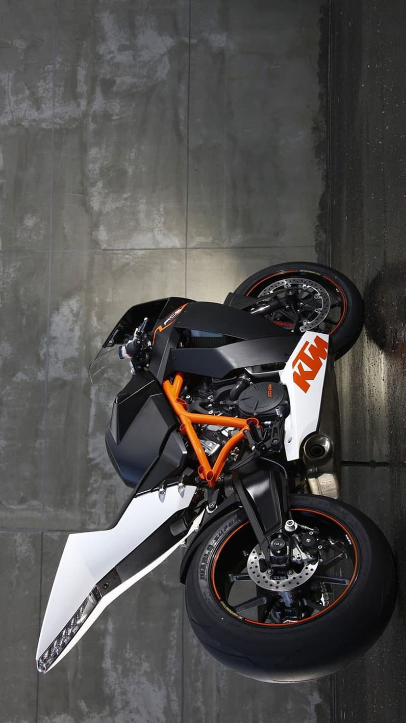 KTM Super Duke R motorbike featuring an orange frame and black accents parked beside a weathered concrete wall.