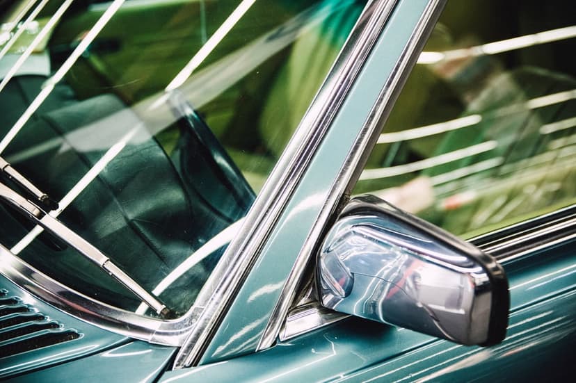 Teal vintage car side mirror and chrome windshield trim show reflections in a vertical close-up composition.