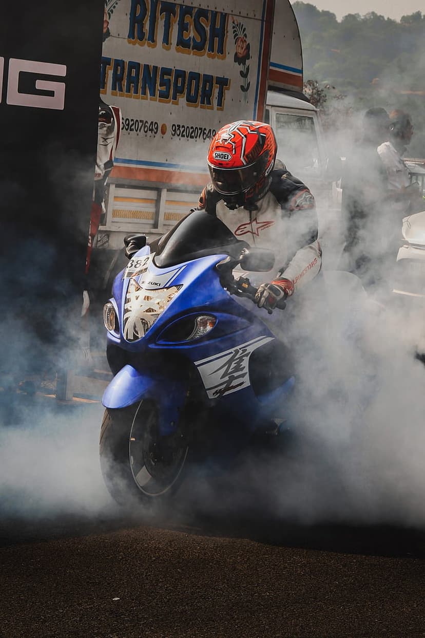 Suzuki Hayabusa motorcycle rider in a white racing suit performs a smoky burnout next to a transport truck.