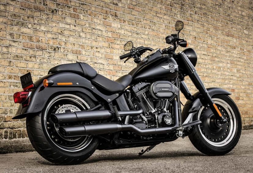 Black Harley-Davidson motorcycle parked against a tan brick wall with solid silver rims and dual exhaust pipes.