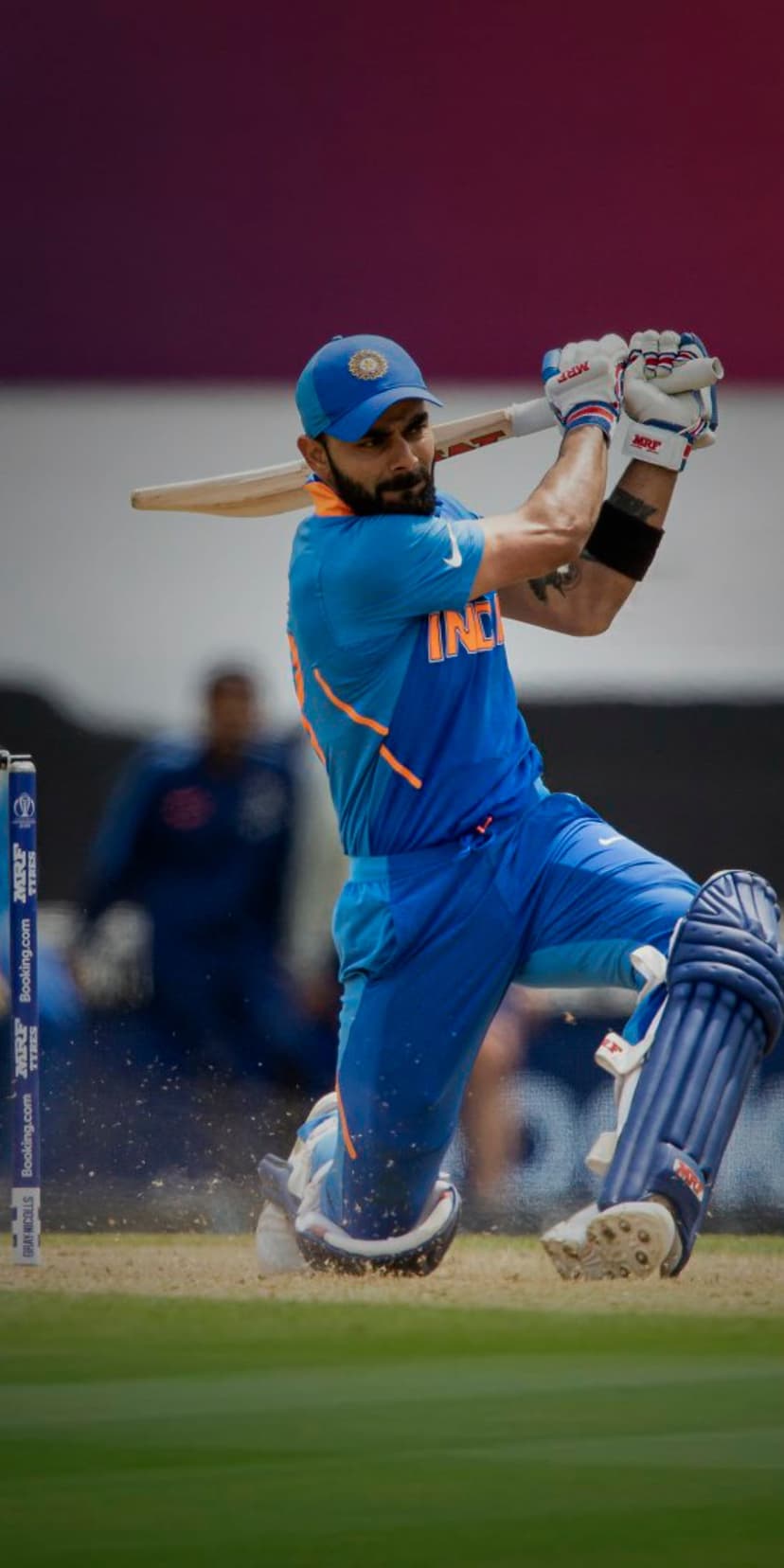 Virat Kohli grips his cricket bat during an intense match play, wearing a blue jersey and white protective pads.