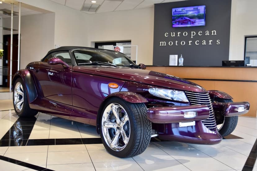 Metallic purple Plymouth Prowler with chrome wheels on a tiled showroom floor under bright indoor lighting.