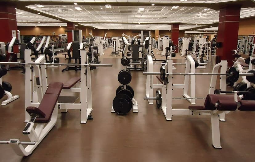 White weightlifting benches and barbells line a polished gym floor with red pillars and bright overhead lights.