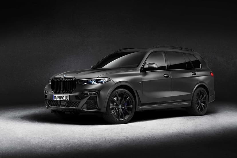 Matte grey BMW X7 SUV in a dark studio with blue headlights and black wheels on a lit concrete floor.