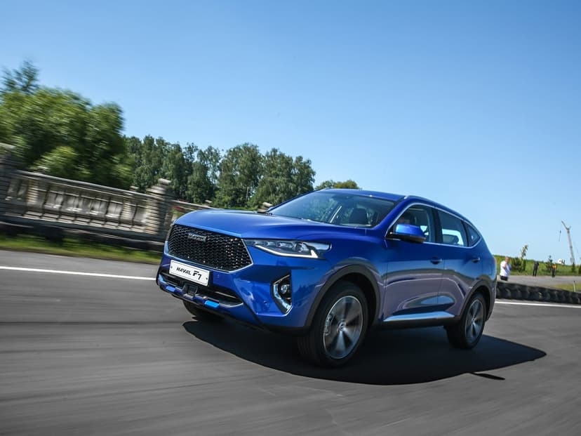 Blue Haval F7 SUV driving on an asphalt road with motion blur, green trees, and a clear blue sky background.