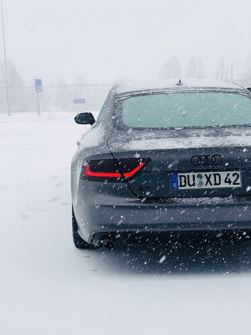 Audi A7 rear view with glowing red taillights and 'DU XD 42' license plate during a heavy winter snowfall at night.