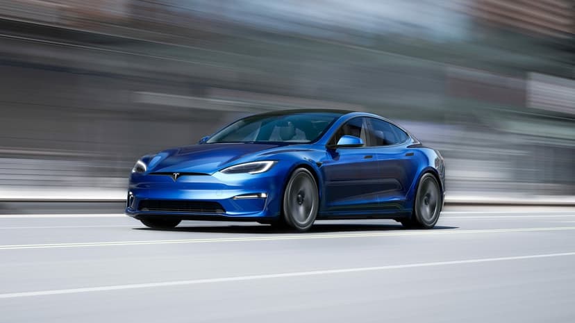 Blue Tesla Model S Plaid electric sedan driving at high speed with motion blur on an urban road landscape.