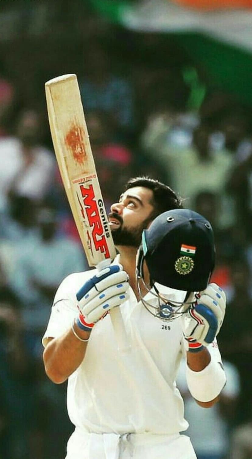 Virat Kohli raises a cricket bat and helmet with a triumphant gaze during a victory celebration on the pitch.