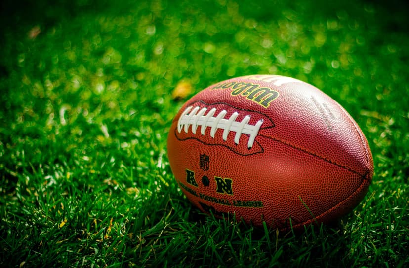 American football with white laces lies on a bright green grass field with a shallow depth of field.