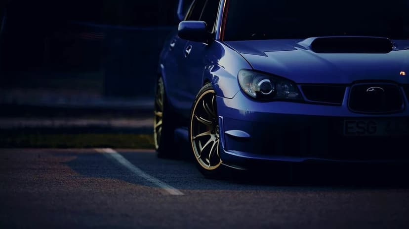 Blue Subaru WRX STI with gold wheels parked on asphalt at night with shallow depth of field and soft lighting.